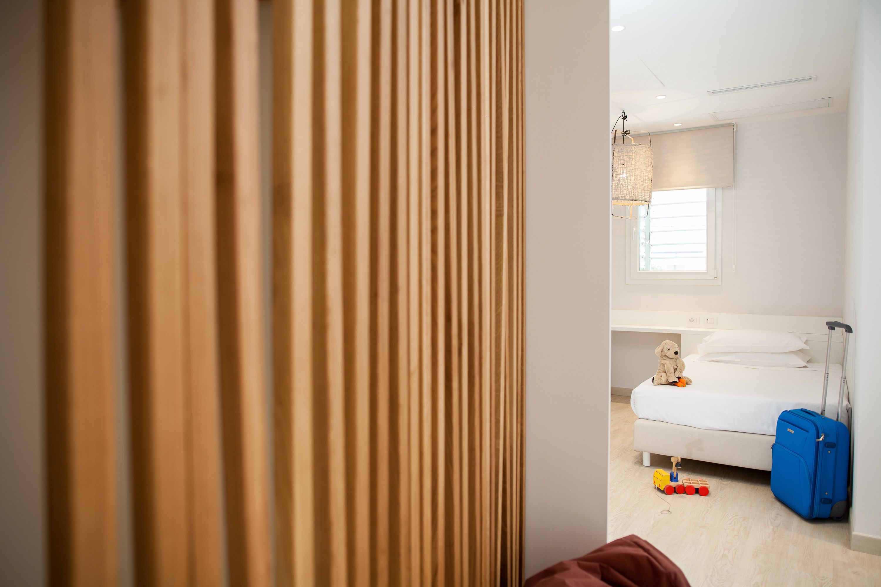 Une chambre d’hôtel avec un lit, une valise et des jouets éparpillés sur le sol.