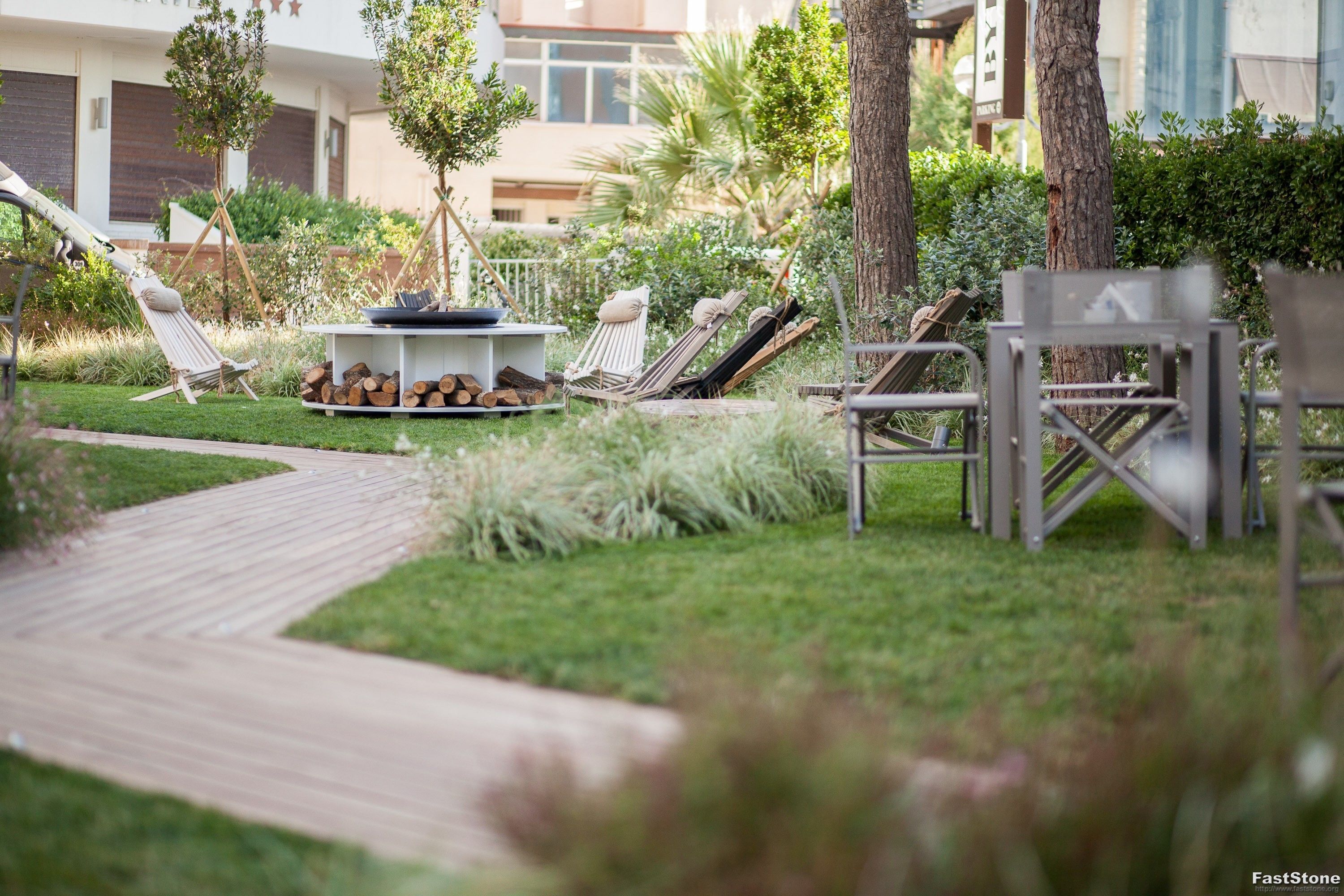 A well-maintained outdoor area with a wooden deck, lounge chairs, and a small table with logs.