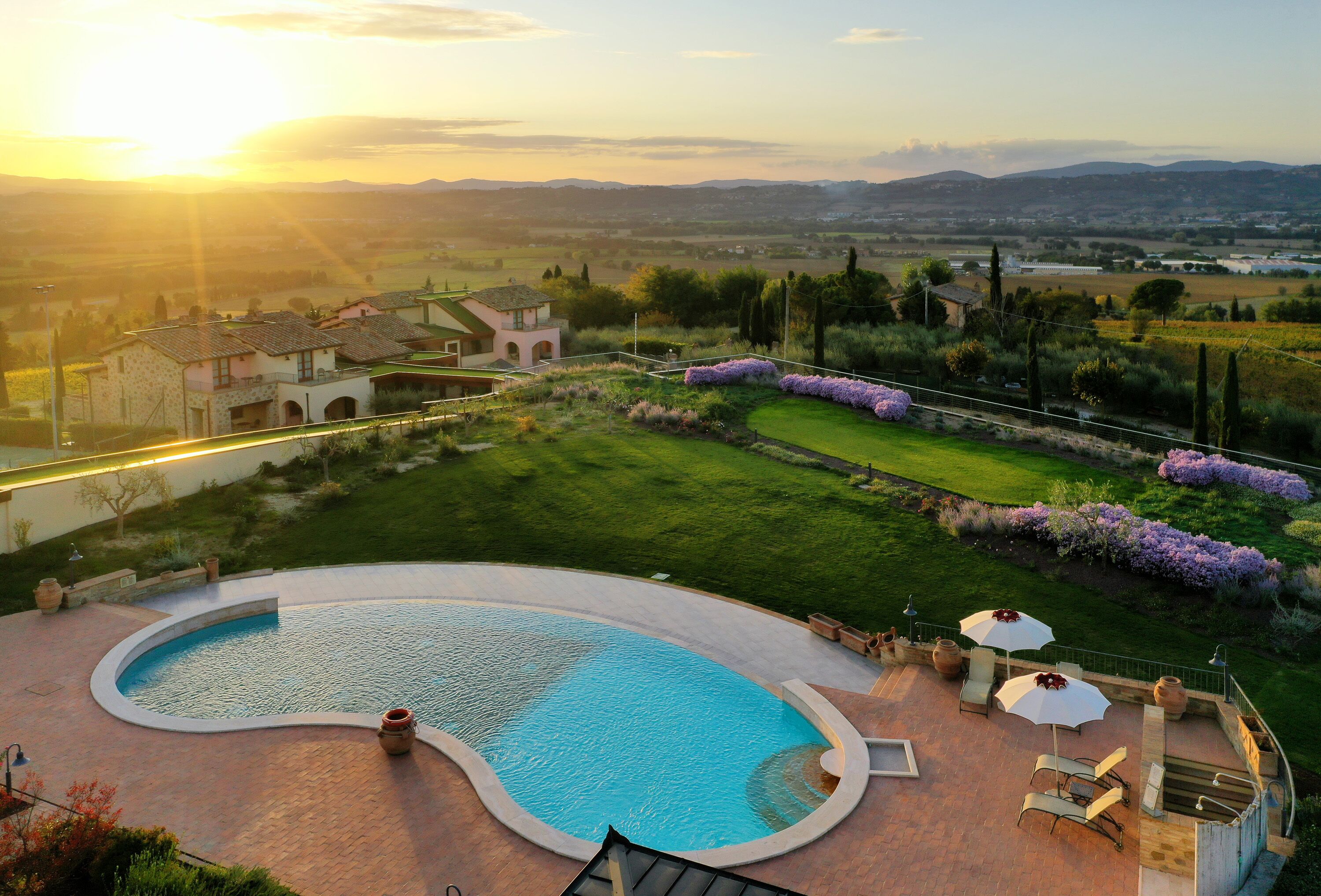 Una piscina de borde curvo, rodeada por una terraza con mobiliario exterior y vistas a un paisaje rural al fondo.