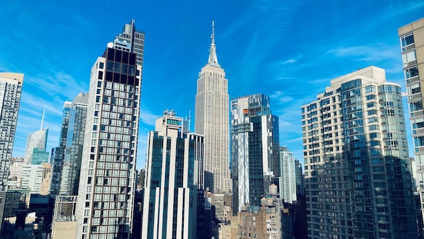 Un paysage urbain avec des immeubles modernes de grande hauteur, dont un gratte-ciel remarquable surmonté d’une flèche.