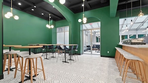Un café moderno con paredes verdes, mesas de madera y un suelo con estampado blanco y negro.