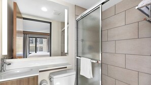 Une salle de bain moderne avec une douche à parois de verre, des toilettes blanches et un lavabo surmonté d’un miroir.
