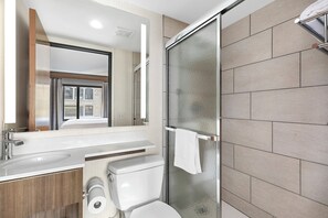 Une salle de bain moderne avec une douche à parois de verre, des toilettes blanches et un lavabo surmonté d’un miroir.