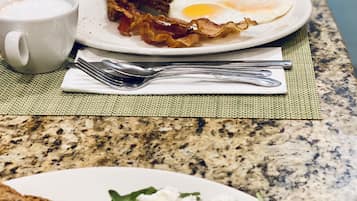 A breakfast setting with a plate of eggs, bacon, and toast, a cup of coffee, and a glass of orange juice on a granite countertop.