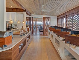 Un área de bufé con distintas estaciones de comida, paneles de madera y vista al mar.