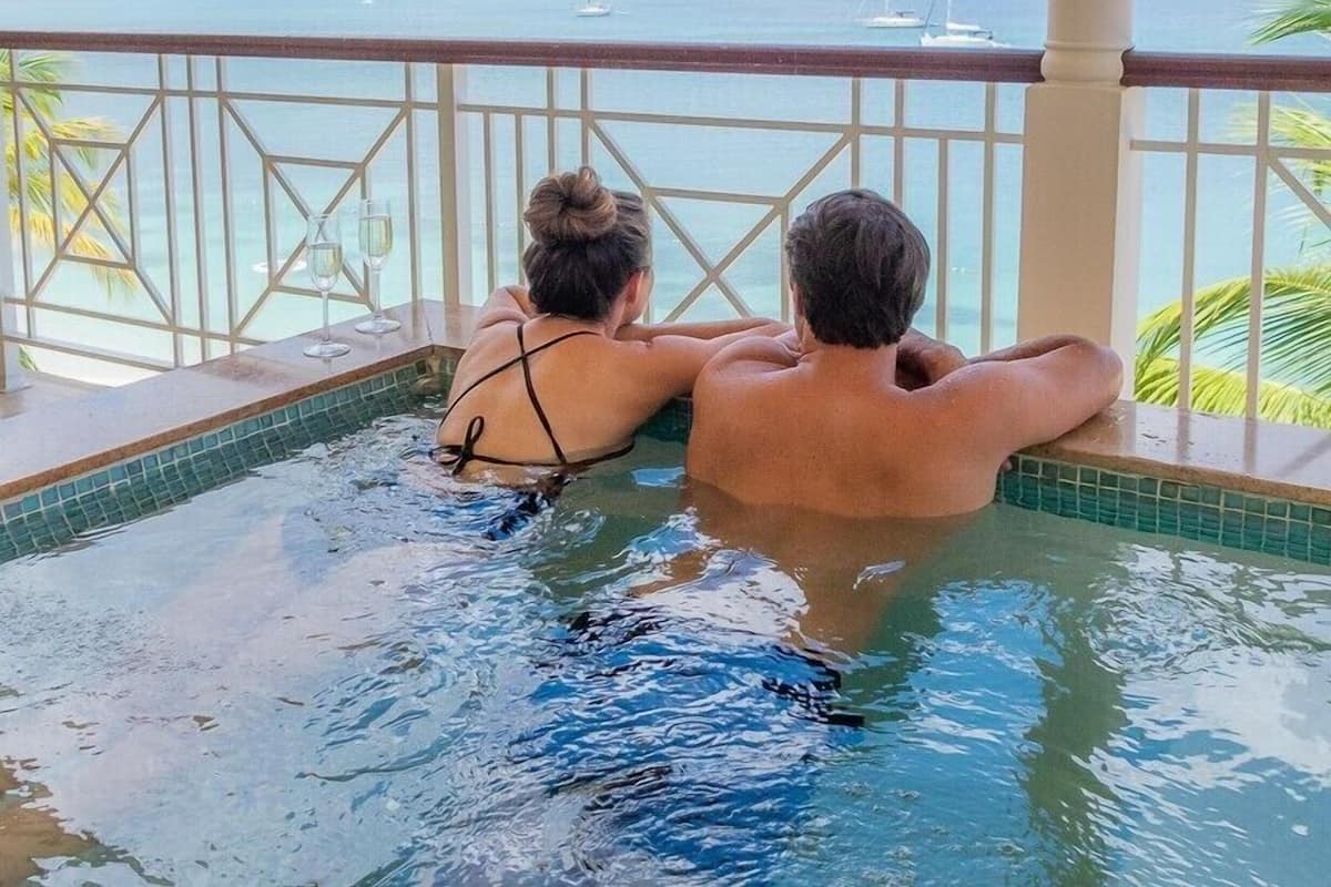 A couple relaxing in a hot tub with a view of the sea and mountains.