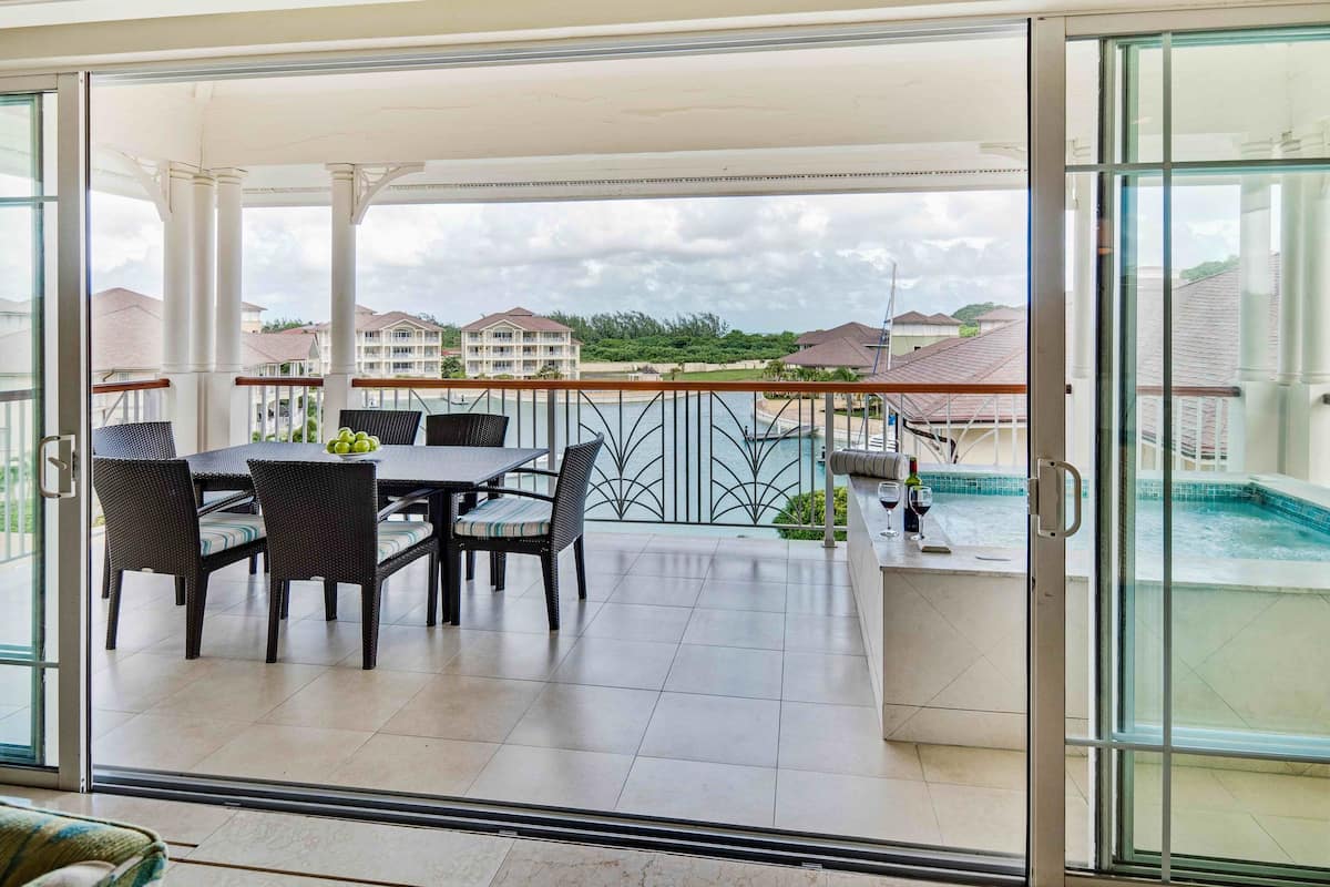 A balcony with a table and chairs, a pool, and a view of other buildings.