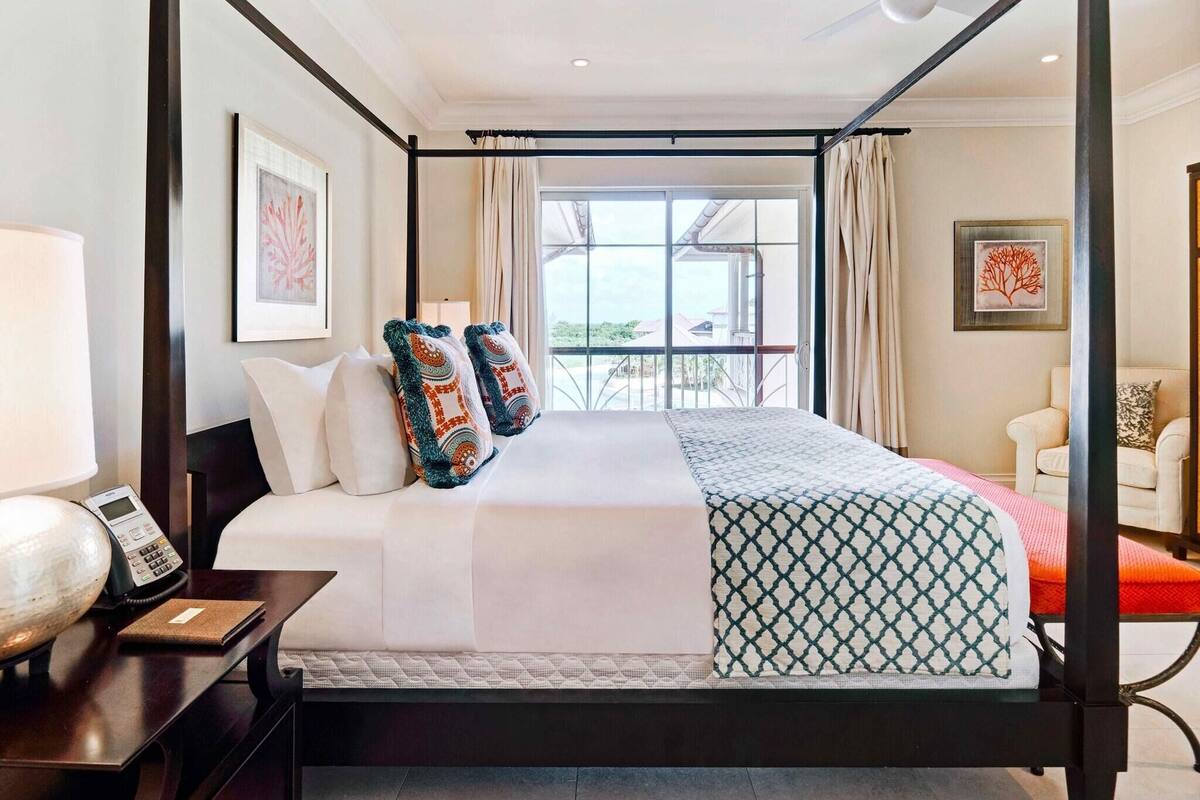 A four-poster bed with a view of the outdoors, a bedside table with a lamp, and a chair in the corner.