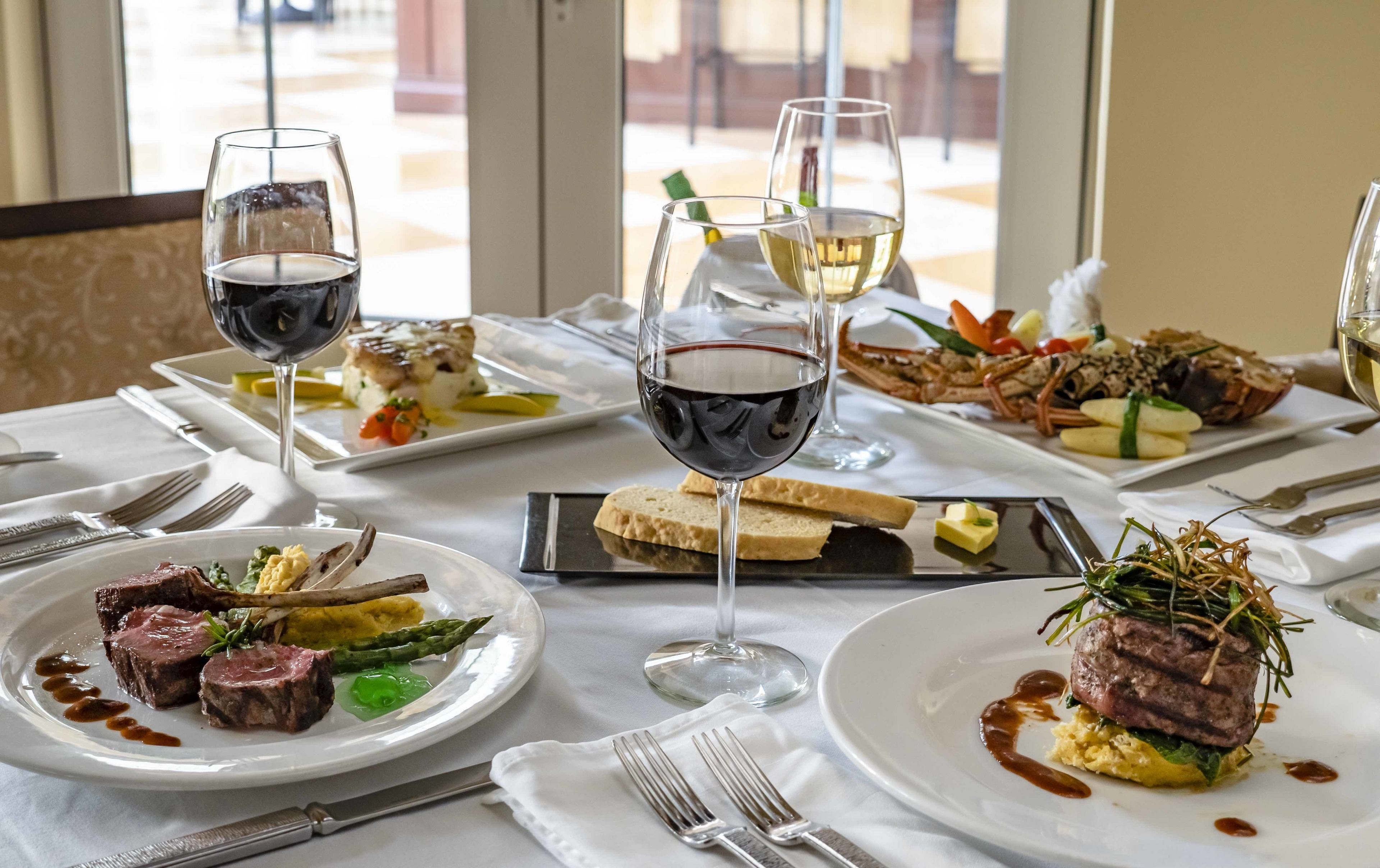 A dining table with multiple plates of food, glasses of wine, and cutlery.