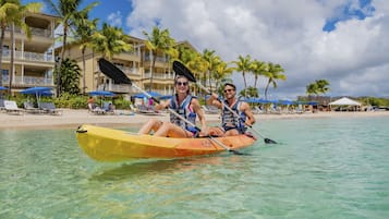 Um casal pratica caiaque em um mar azul-turquesa calmo, com um resort ao fundo.