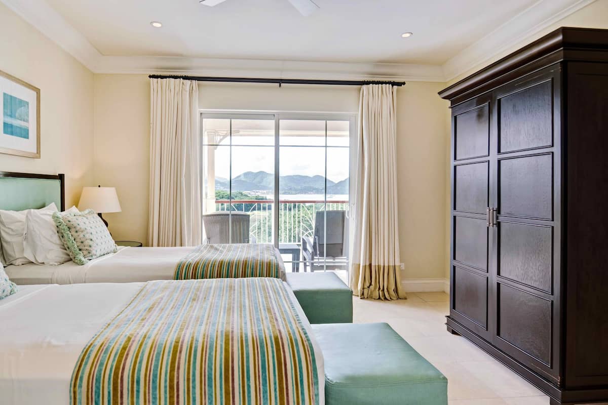 A hotel room with two beds, a large wardrobe, a balcony with a view of the mountains, and a table with chairs outside.