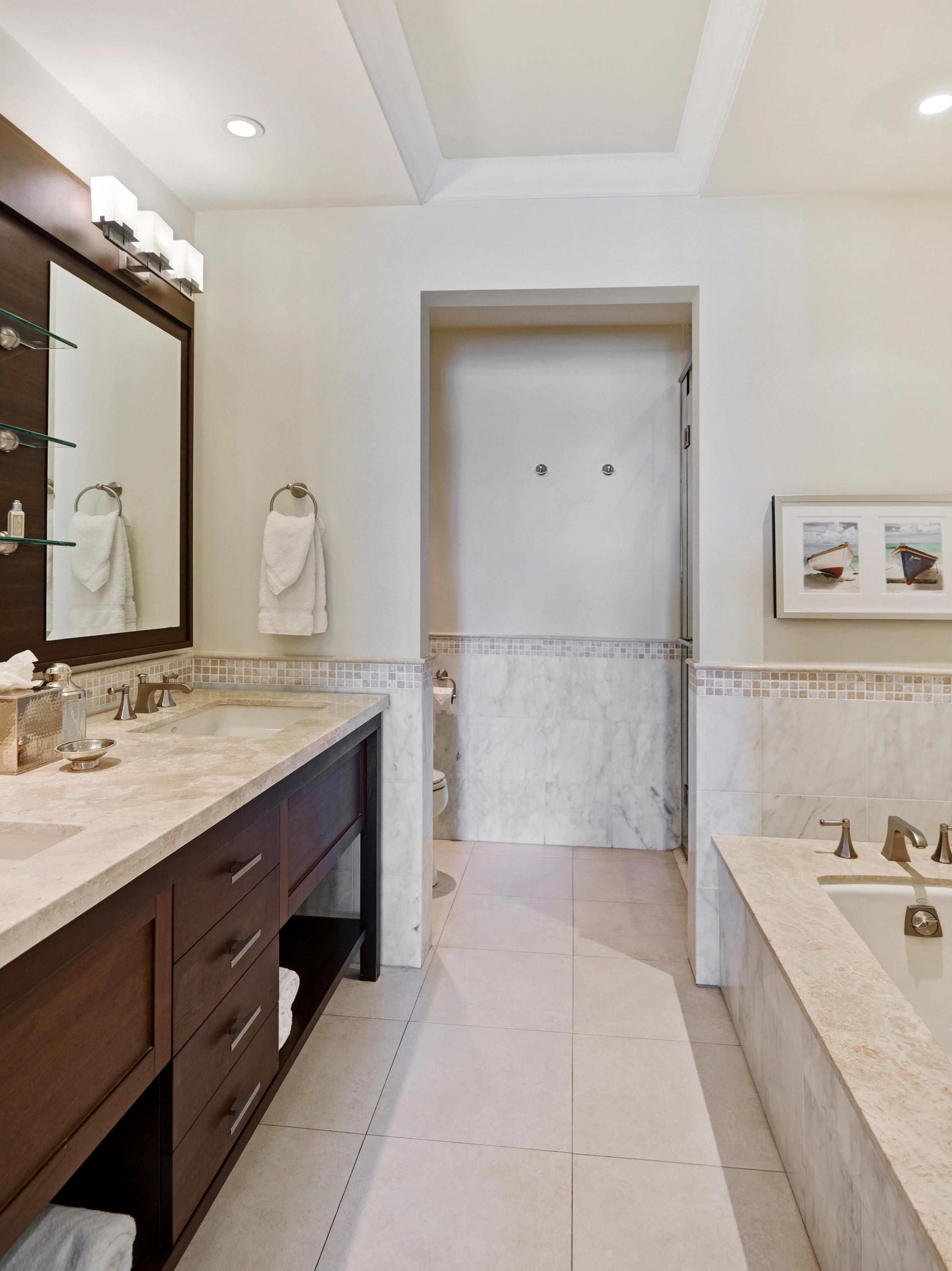 A modern bathroom with a large mirror, dual sinks, and a walk-in shower.