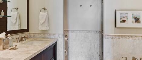 A modern bathroom with a large mirror, dual sinks, and a walk-in shower.