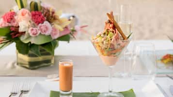 A table set with a glass of a pinkish drink, a clear glass with a pink drink, a plate with a green leaf, and a floral arrangement.