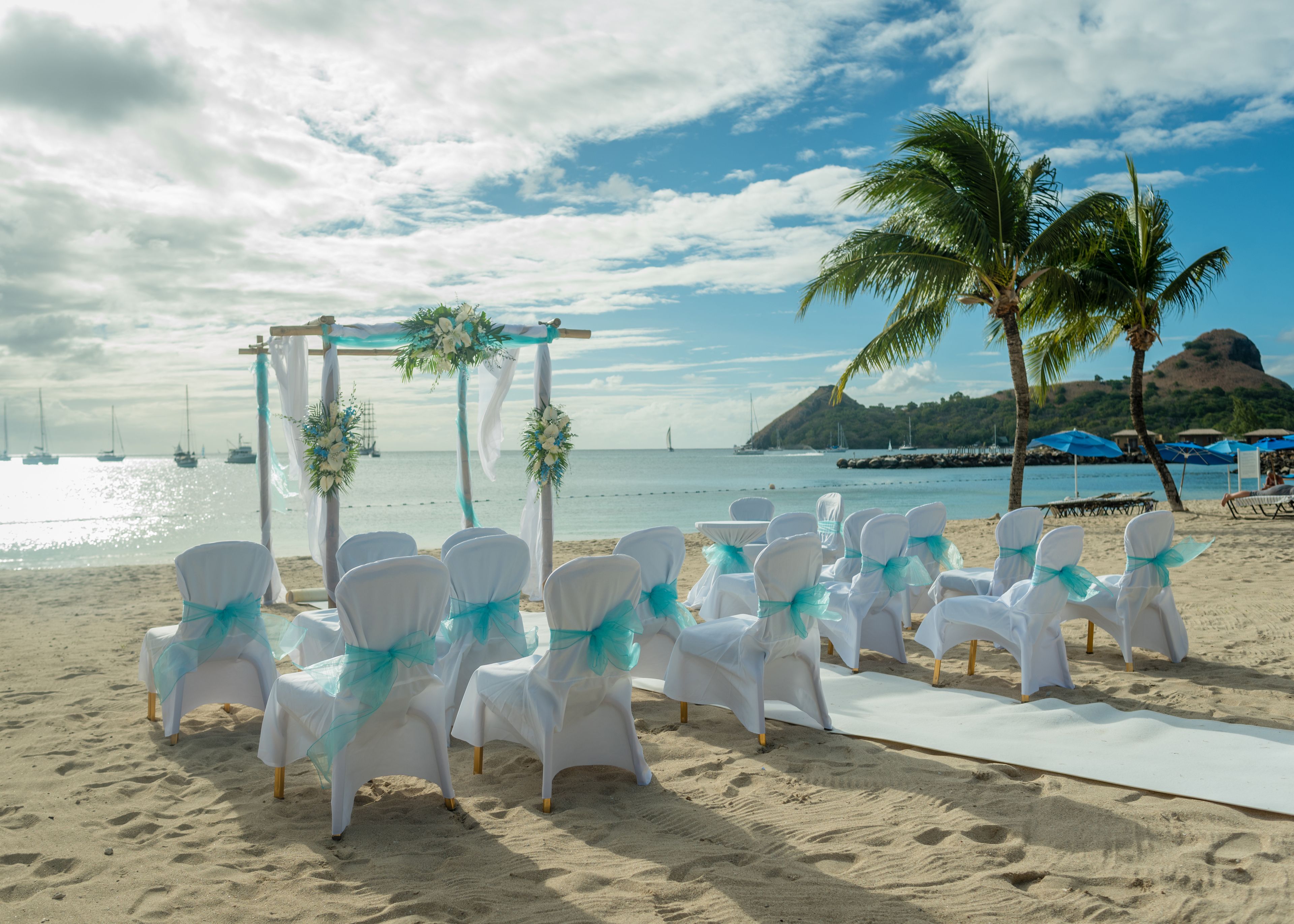 A beach wedding setup with white chairs and a white aisle.