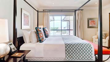 Una cama con dosel con almohadas estampadas, una mesita de noche con lámpara y teléfono, y vistas al exterior a través de amplias ventanas.
