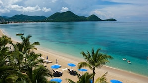 A beach with clear turquoise water, palm trees, and a distant mountain range. - The Landings Resort & Spa (Gros Islet)