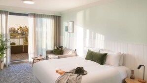 A hotel room with a large bed, a small table, a chair, and a balcony with a view of palm trees. - The Sebel Kiama (Kiama)