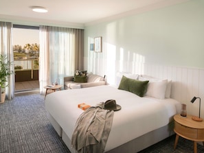 A hotel room with a large bed, a small table, a chair, and a balcony with a view of palm trees. - The Sebel Kiama (Kiama)