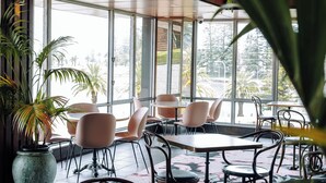 A spacious indoor area with large windows, multiple tables and chairs, and potted plants. - The Sebel Kiama (Kiama)