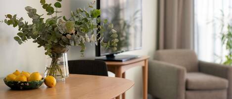 Et spisebord med en vase blomster og citroner, et fjernsyn og en sofa i en stue.