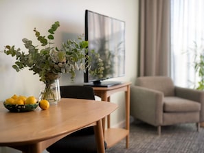 A dining table with a vase of flowers and lemons, a television, and a sofa in a living area. - The Sebel Kiama (Kiama)