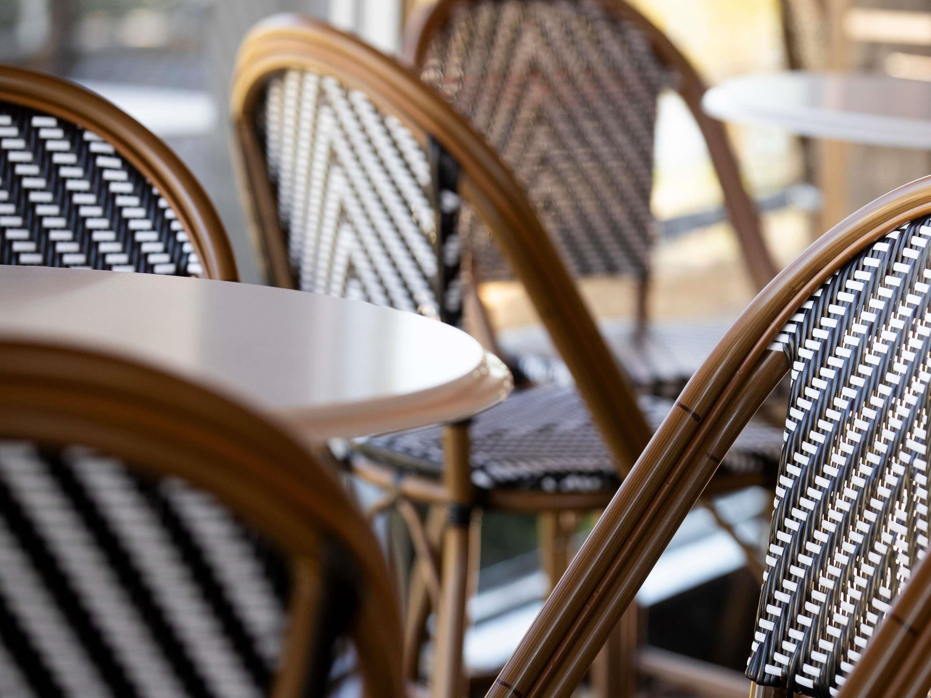 Sillas de mimbre con respaldos trenzados y asientos acolchados, dispuestas alrededor de mesas redondas en un café.