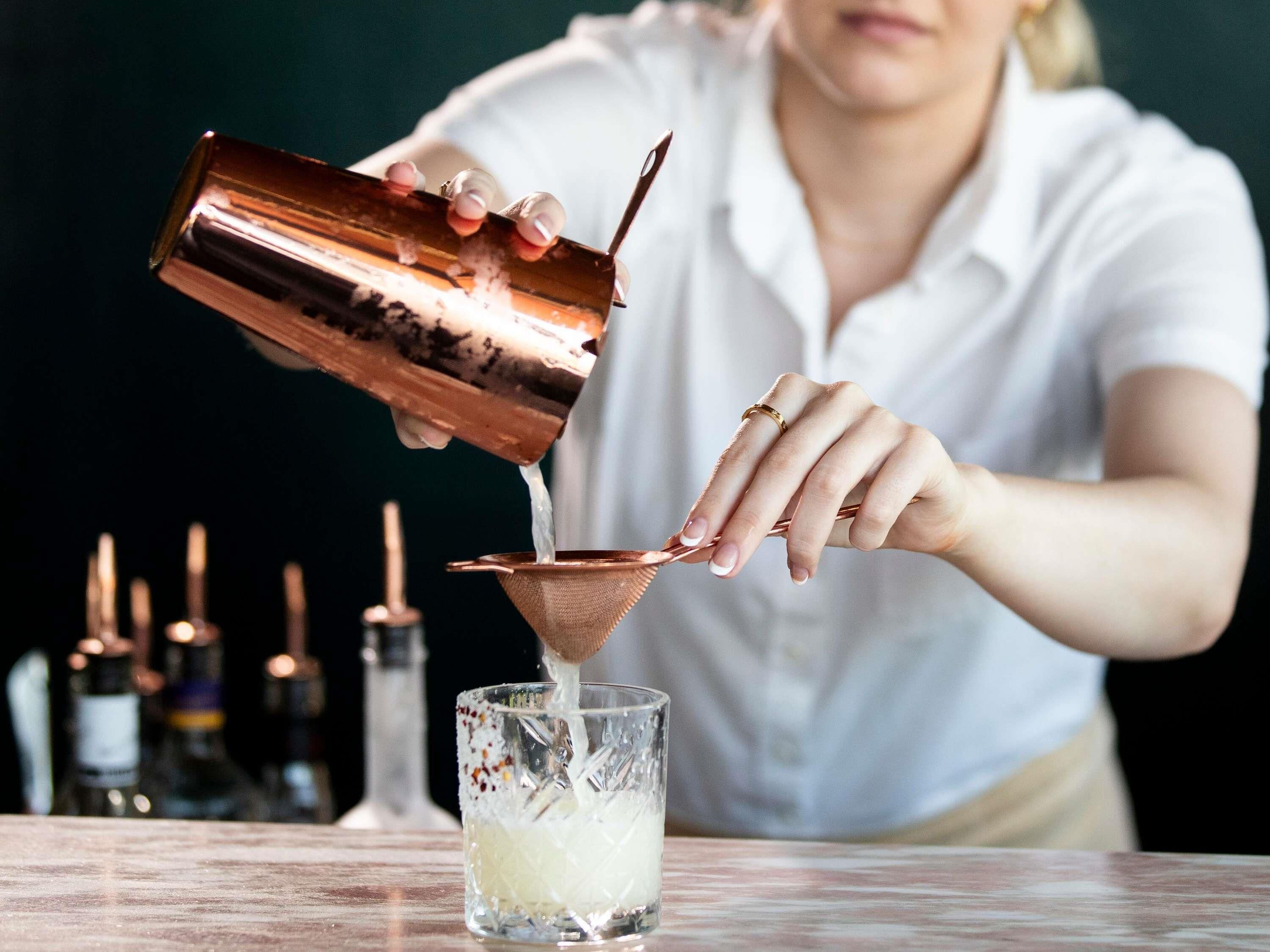 Eine Person gießt eine Flüssigkeit aus einem Kupferbehälter in ein Glas.