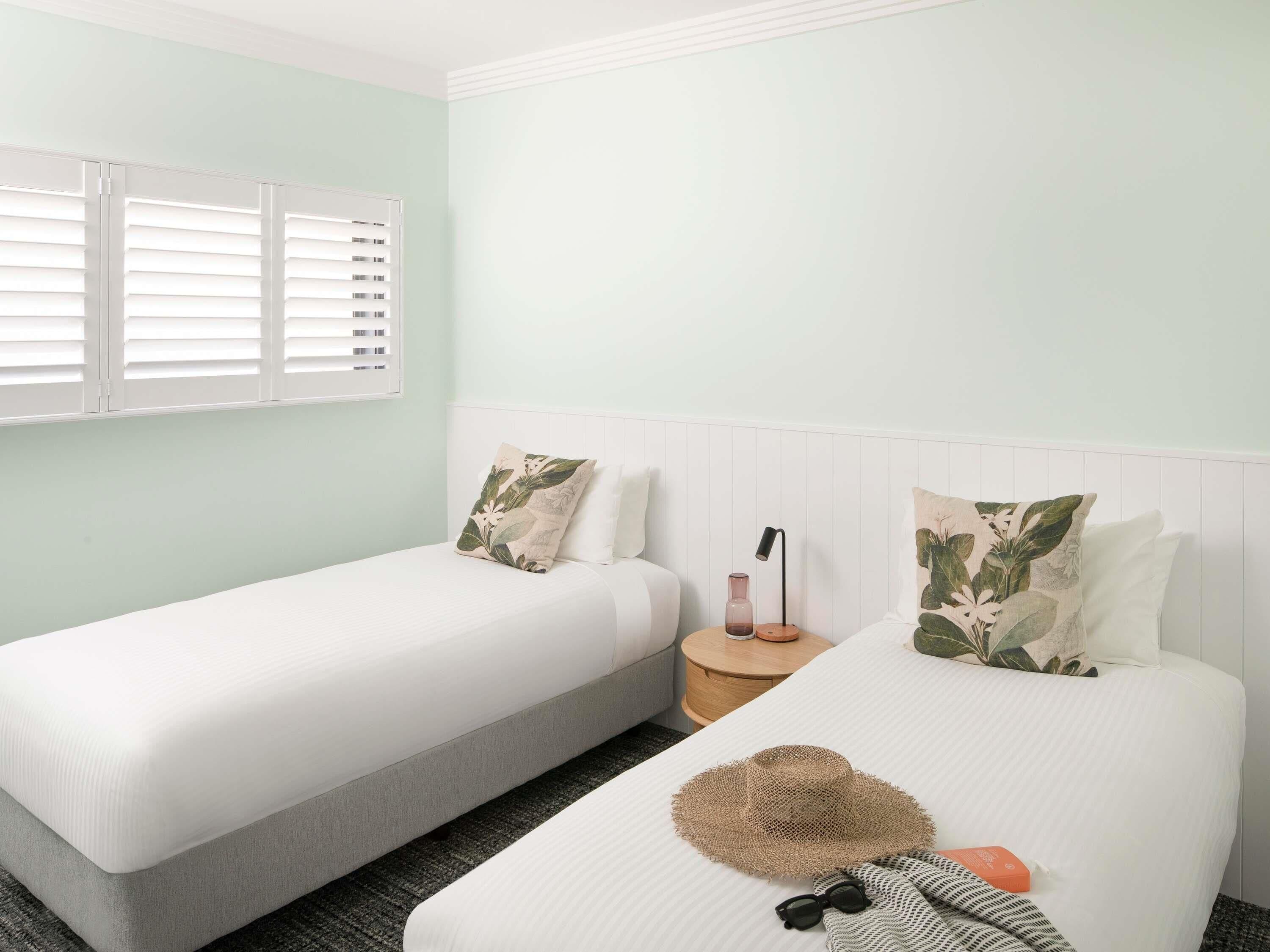 A room with two beds, a nightstand, a lamp, and a window with blinds.