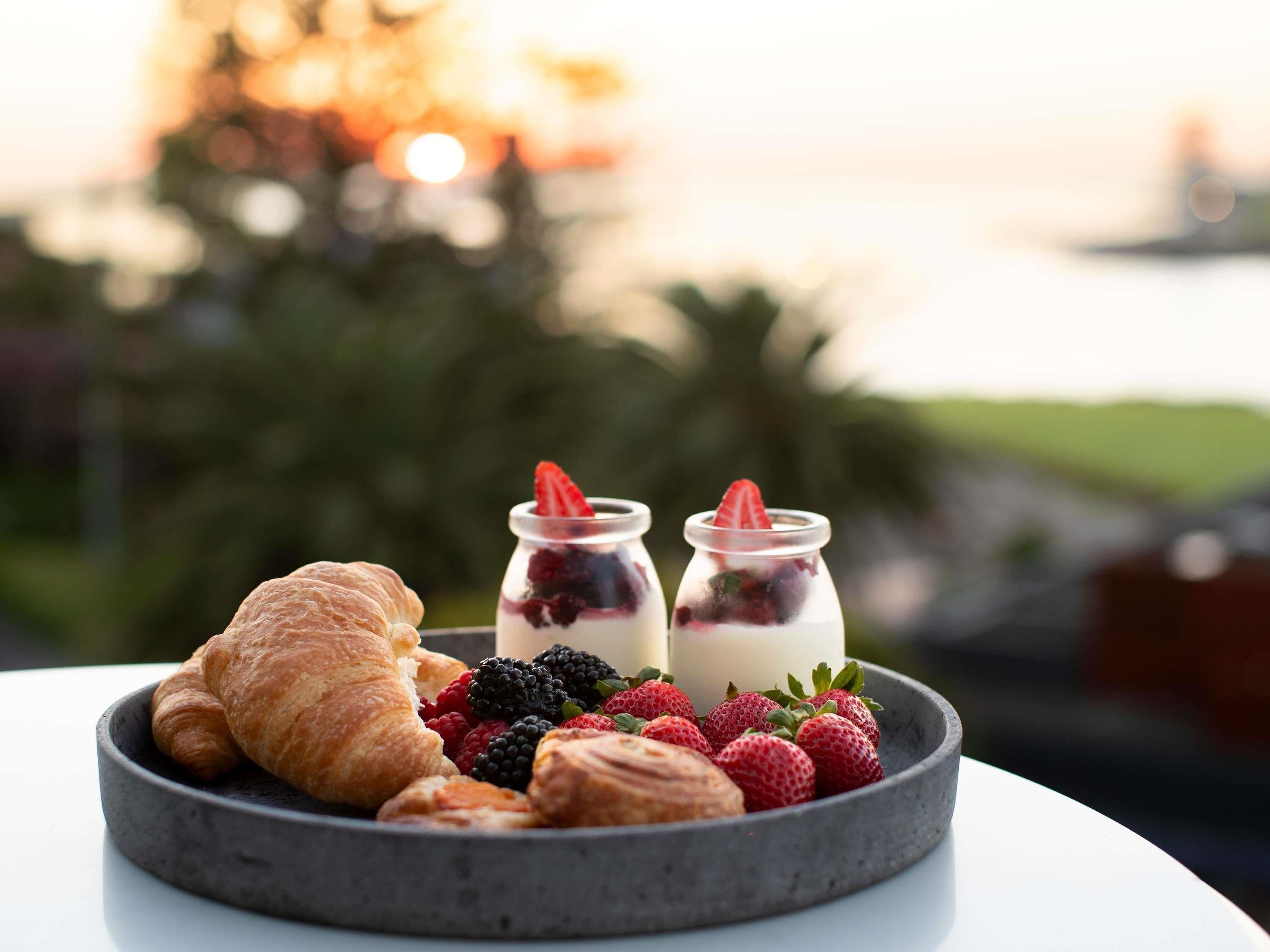 Un desayuno con cruasanes, fresas, frambuesas y dos vasos de yogur con frutos rojos.