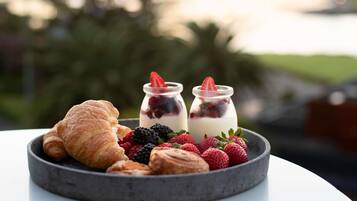 Un desayuno con cruasanes, fresas, frambuesas y dos vasos de yogur con frutos rojos.