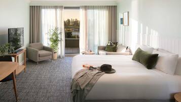 Ein Hotelzimmer mit einem großen Bett, einer Sitzecke, einem Schreibtisch mit Fernseher und einem Balkon mit Vorhängen.