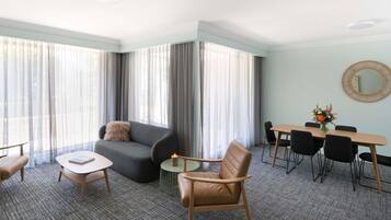 Een hotelkamer met een bank, een klein rond tafeltje, een eettafel met stoelen en een grote spiegel aan de muur.