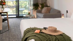 A hotel room with a bed, a small table with a candle, a sofa, and a view of greenery outside. - The Sebel Kiama (Kiama)