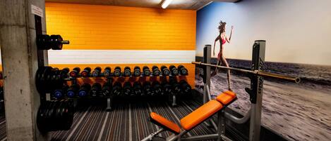 A gym with a bench press, multiple dumbbells, and a wall mural.