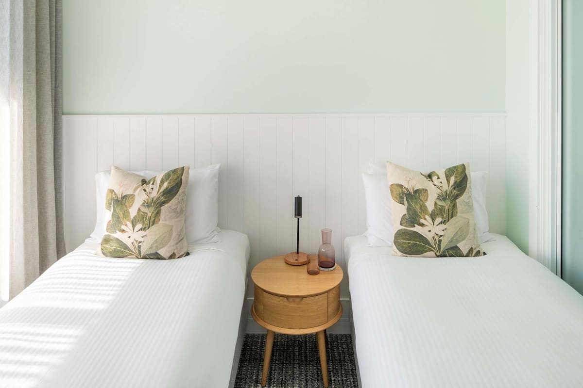 A hotel room with two single beds, a round wooden nightstand, and a white headboard.