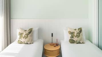 A hotel room with two single beds, a round wooden nightstand, and a white headboard.