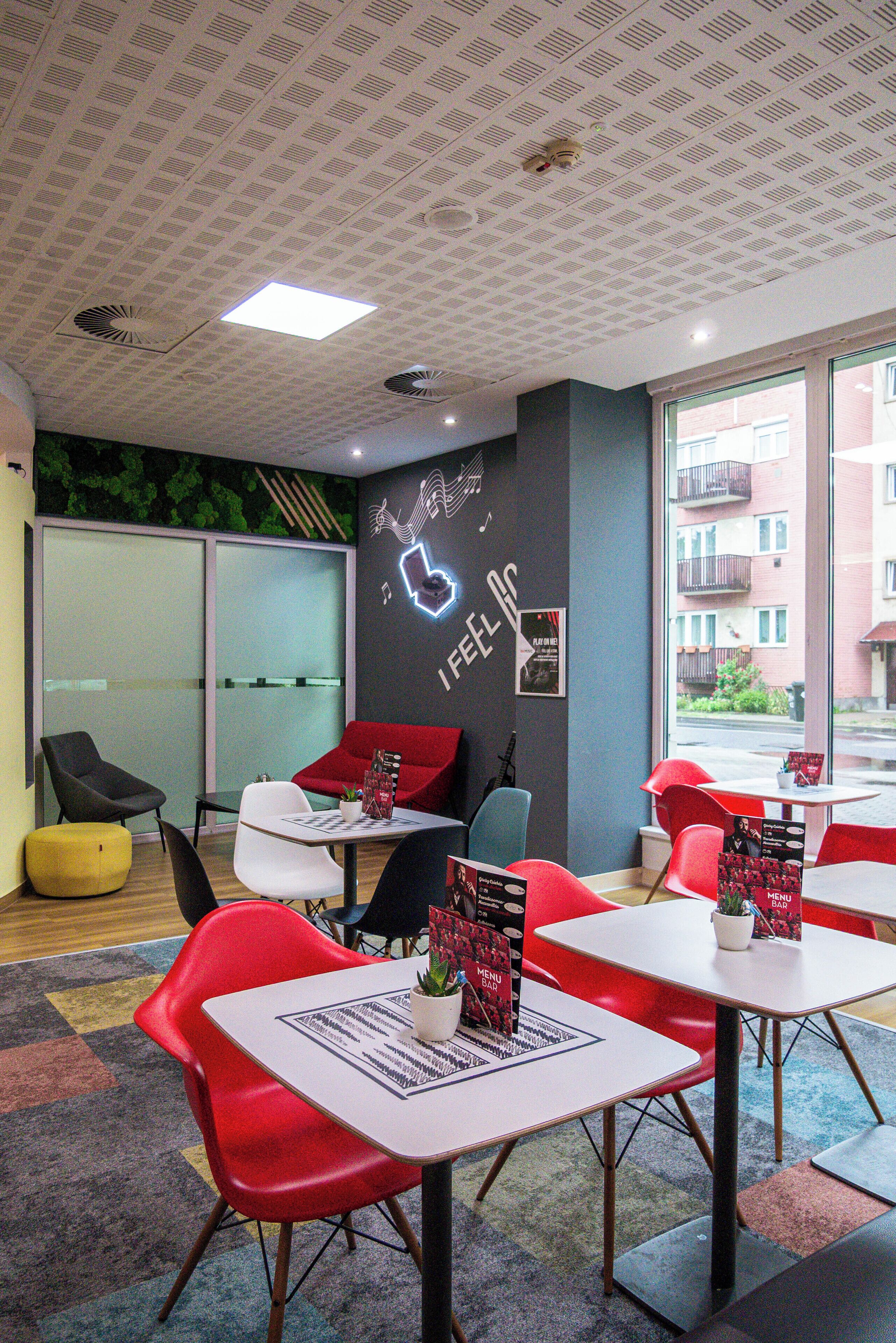 A modern office space with red and black chairs, white tables, and a large window offering a view of buildings.
