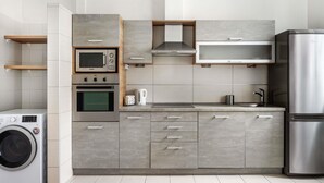 Une cuisine moderne dotée d’appareils électroménagers intégrés, de meubles de rangement gris et d’un réfrigérateur en acier inoxydable.