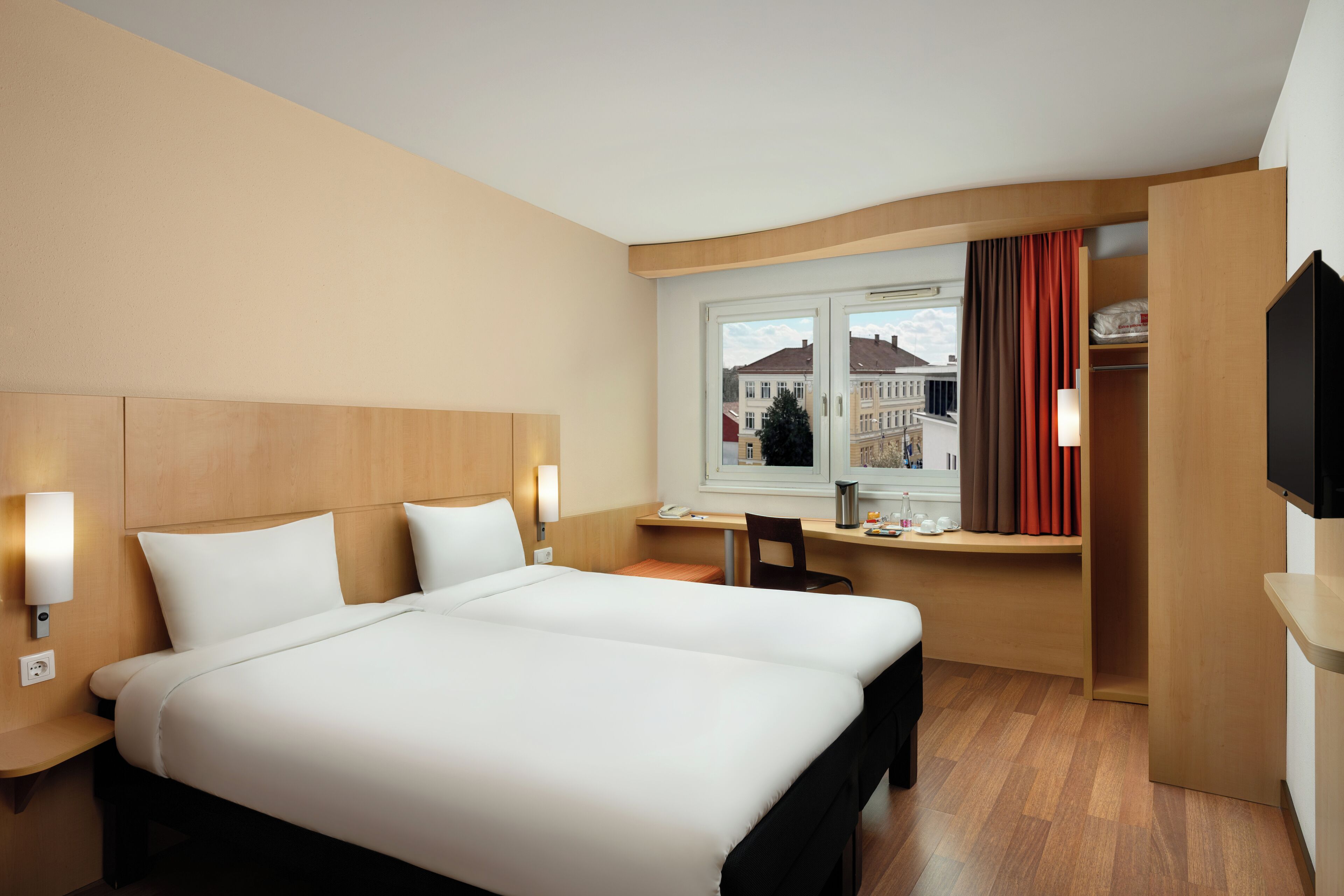 A hotel room with a large bed, a desk, a chair, and a TV.