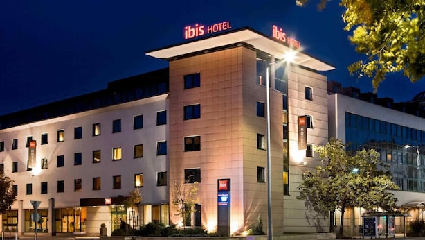 Um hotel moderno com vários andares, um letreiro de destaque com a inscrição "ibis HOTEL" e uma entrada bem iluminada.