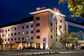 A modern hotel with multiple floors, a prominent "ibis HOTEL" sign, and a well-lit entrance. - ibis Gyor (Gyor)