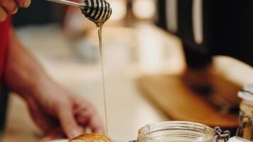A person pouring honey from a jar onto a croissant.