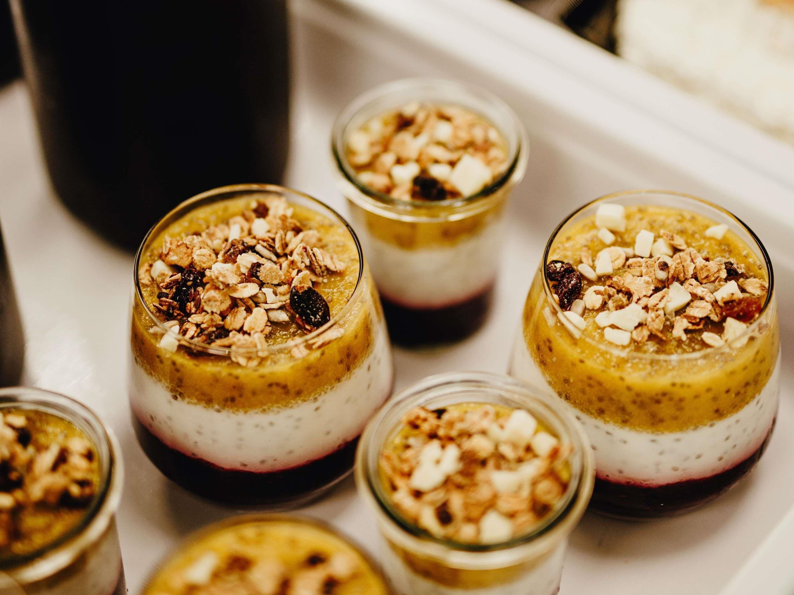 A tray with six glass dessert cups topped with granola and dried fruit.