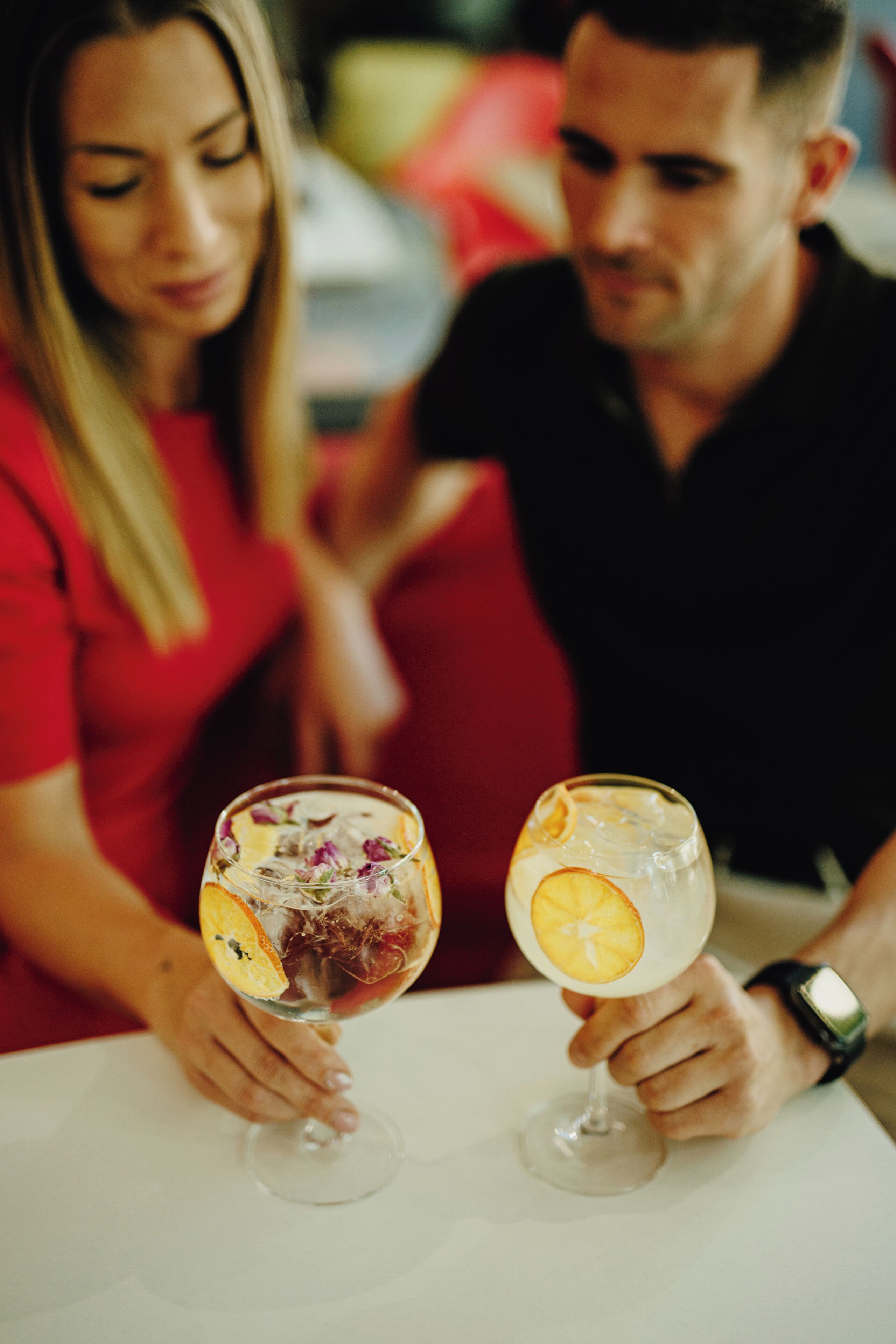 Dos personas sosteniendo vasos con rodajas de fruta, sentadas en una mesa.