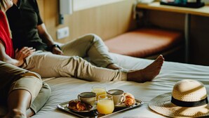 Quarto de hotel com cama, bandeja com itens de café da manhã e uma janela.