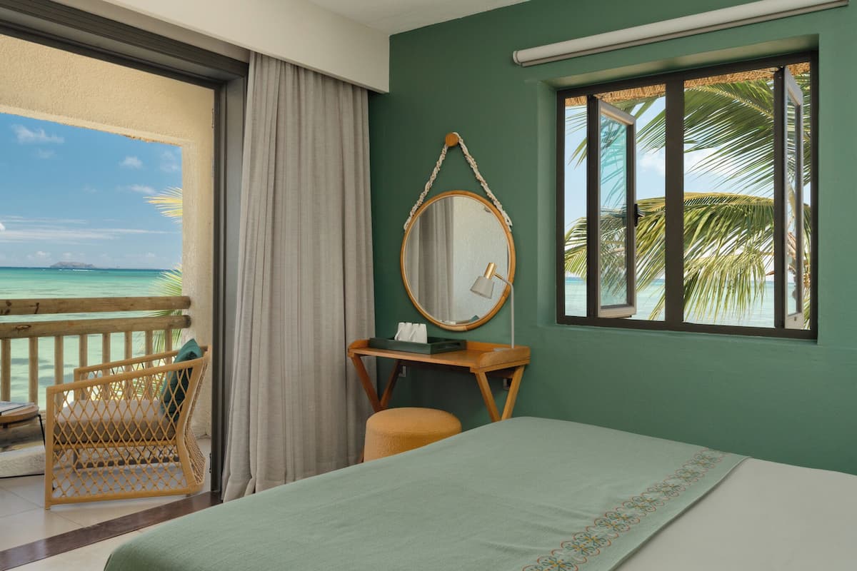 Une chambre d’hôtel avec un lit, un bureau doté d’un miroir, une chaise et une vue sur l’océan.