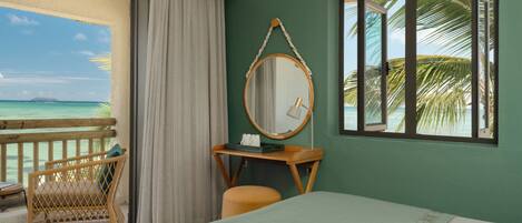 A hotel room with a bed, a desk, a chair, a window with a view of the ocean, and a balcony with a view of the beach.