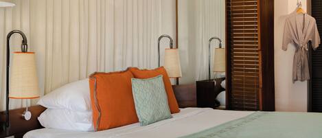A hotel room with a neatly made bed, two bedside lamps, a large mirror, and a robe hanging on the door.