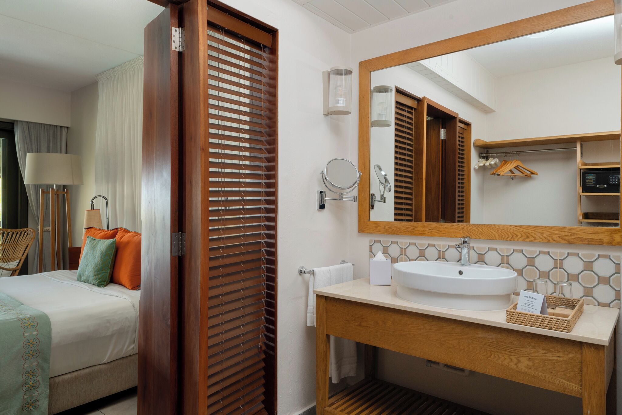 A hotel room with a bed, a wooden door, a bathroom with a sink, mirror, and towel rack.